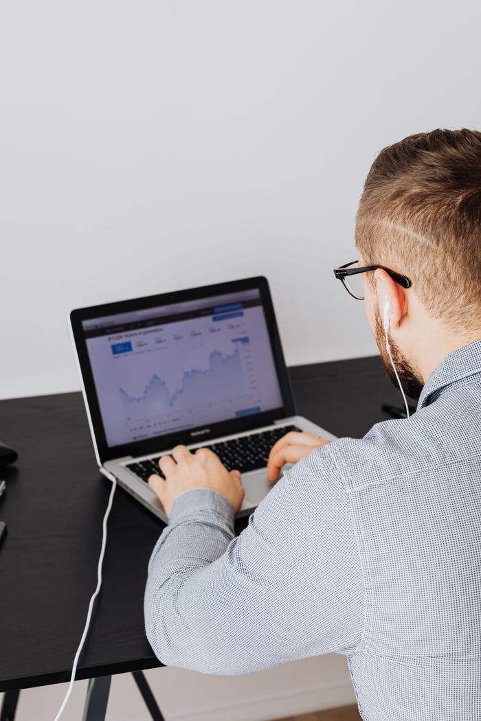 about-us-02 A man uses a laptop indoors to analyze stock market trends graph on screen.